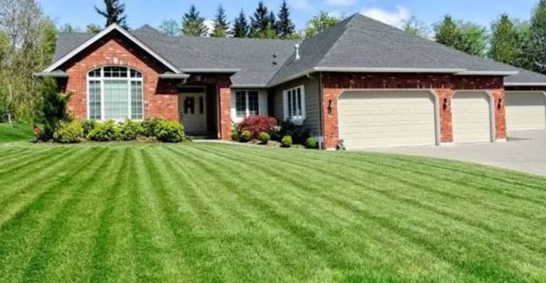 Red brick single-story home with three-car garage and neatly striped green lawn bordered by evergreen trees